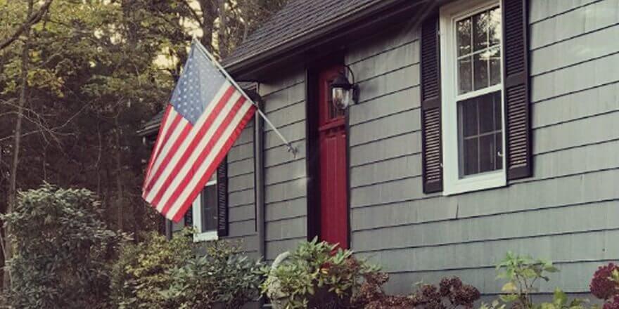A gray home with an American flag flying in front.